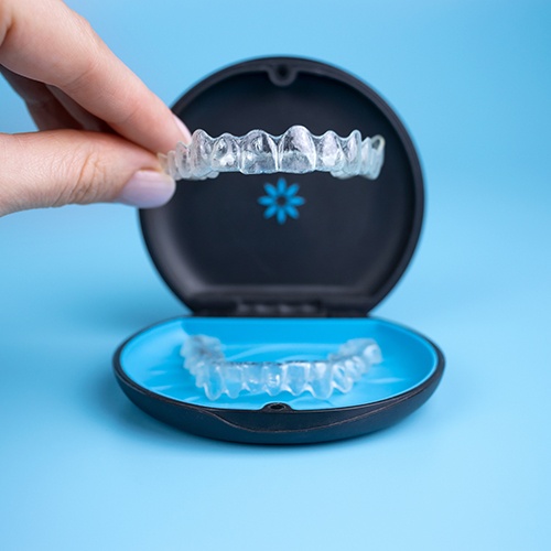 Fingers holding Invisalign tray above its carrier case with light blue background