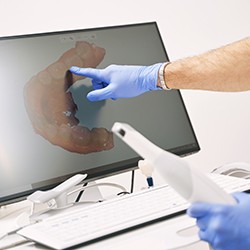 Gloved hands holding digital impression scanner, pointing at computer monitor