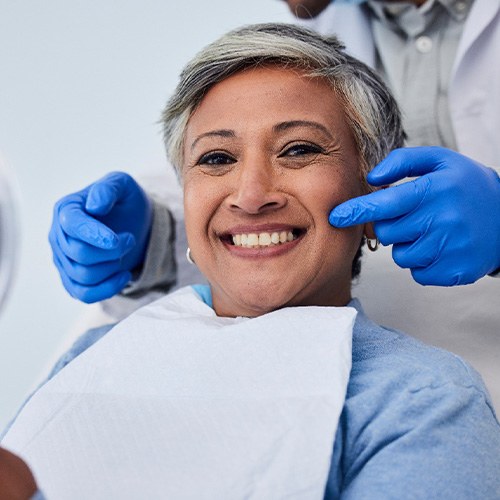 Woman smiling while holding small mirror with dentist